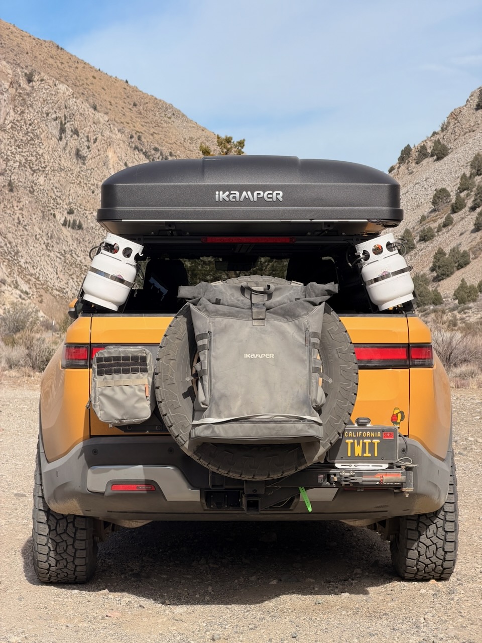 Rear view of the Rivian with a rooftop tent, spare tire, and camp gear
