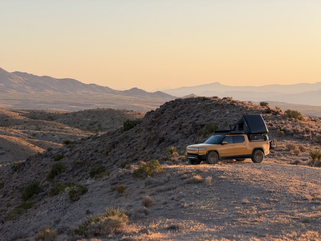 Golden Rivian R1T parked on a desert ridge at sunset
